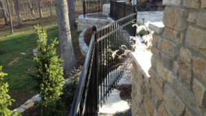 Black ornamental fence installation along a stone wall and landscaped yard, showing an example of fencing cost and design from Elite Fence in Raymore MO.