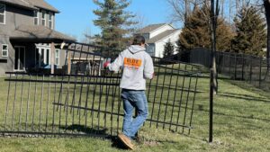 Elite Fence installer carrying a black ornamental fence panel during installation in a residential neighborhood in Raymore MO.