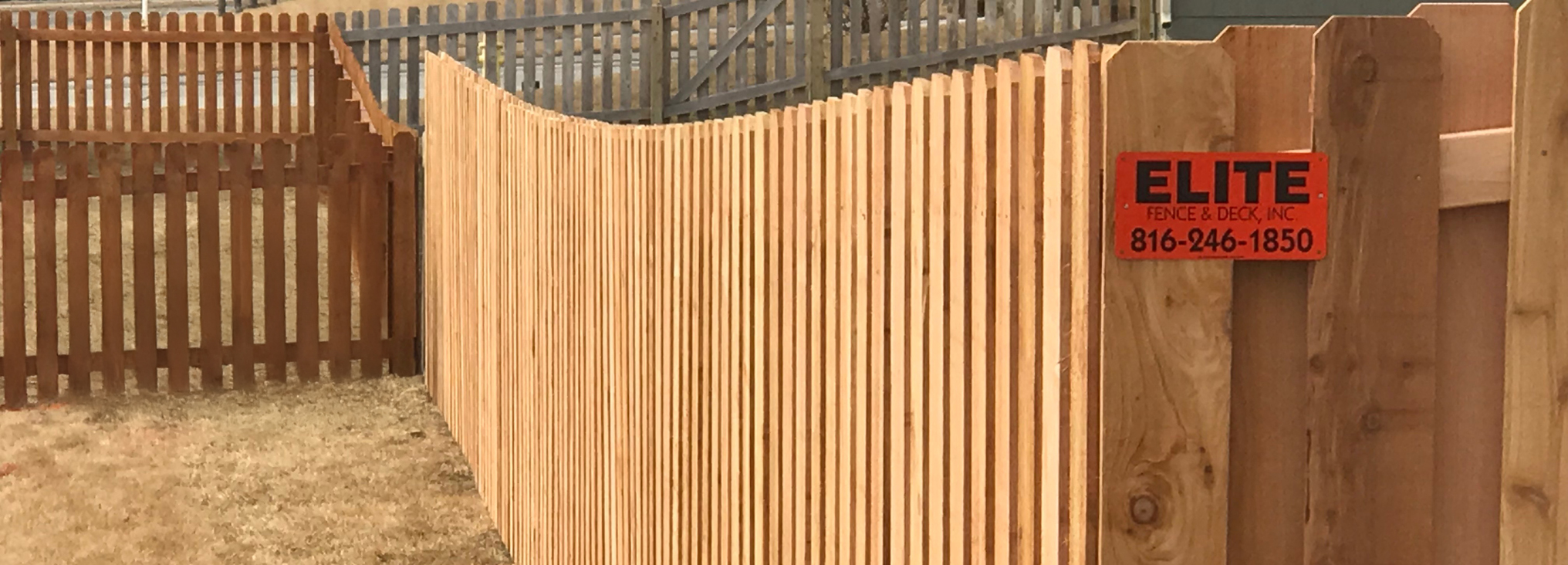 Elite Fence close-up of a custom cedar wood enclosure with vertical pickets and a curved design.