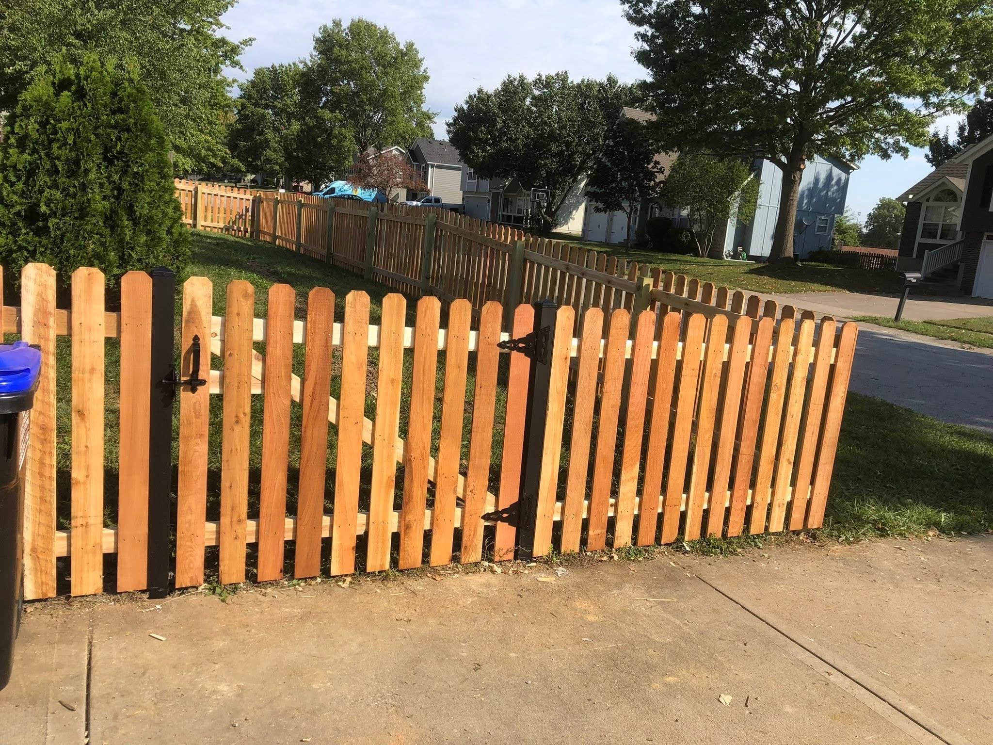 Elite Fence installation of a natural wood picket fence with a convex curved top and a pedestrian gate in a suburban front yard.