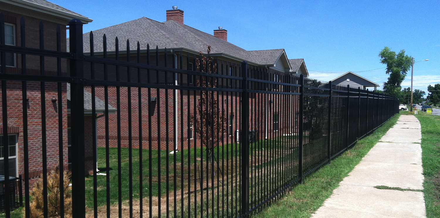 Elite Fence commercial black aluminum ornamental security fence with sharp finials installed along a public sidewalk.