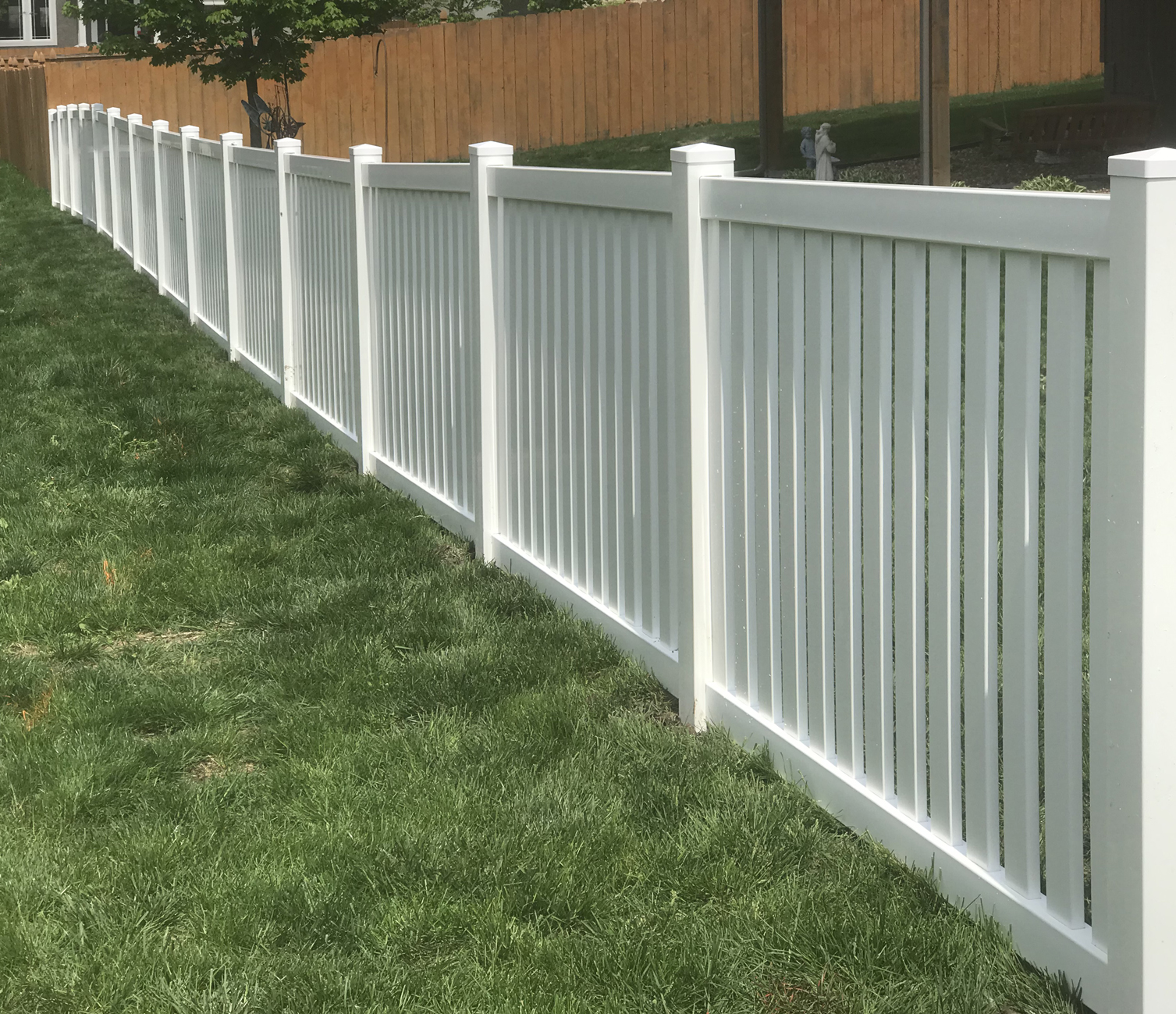 Elite Fence installation of a white vinyl privacy fence along a property line in a residential backyard.
