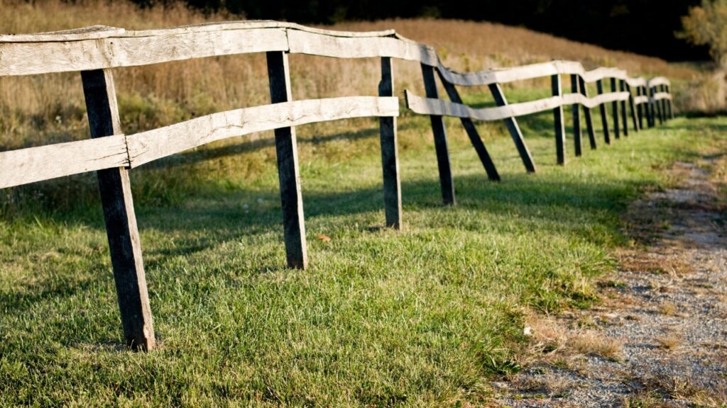 Leaning wooden fence with warped rails and unstable posts showing structural failure before repair.