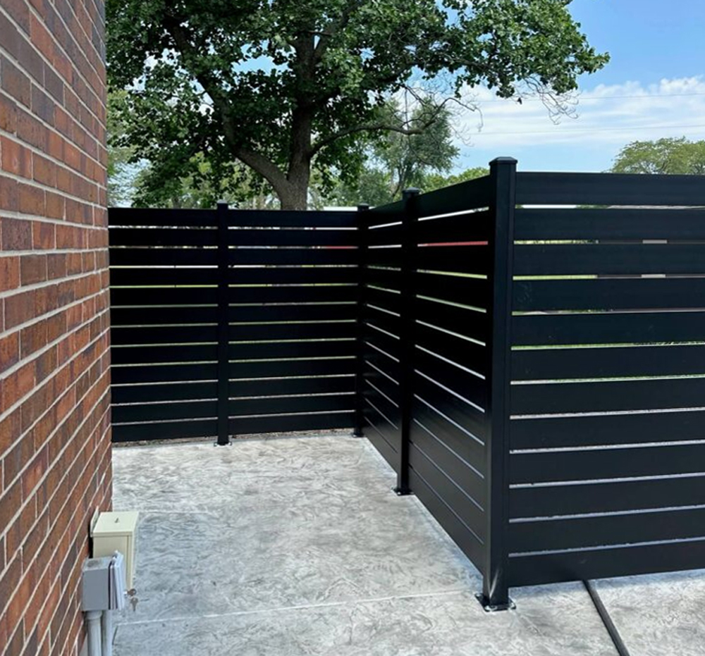Elite Fence black Centurion Select Aluminum horizontal slat screen fence installed against a brick wall for utility enclosure.