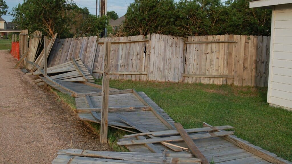 Collapsed wooden garden fence sections lying on grass, highlighting the need for property maintenance and insurance claims.