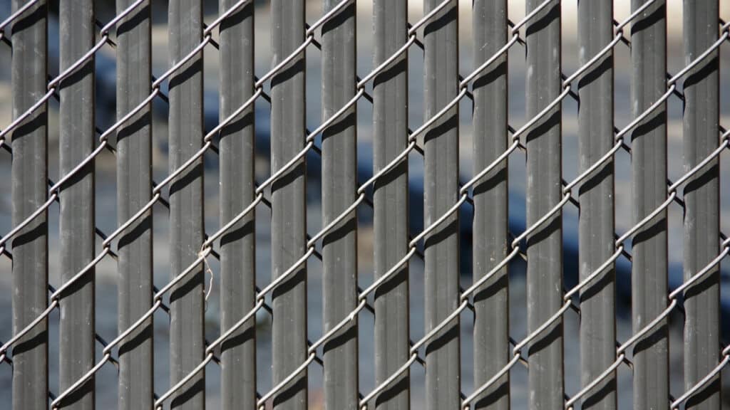Close-up of a black chain link fence featuring privacy inserts, showing a modern way to make a wire fence more private.