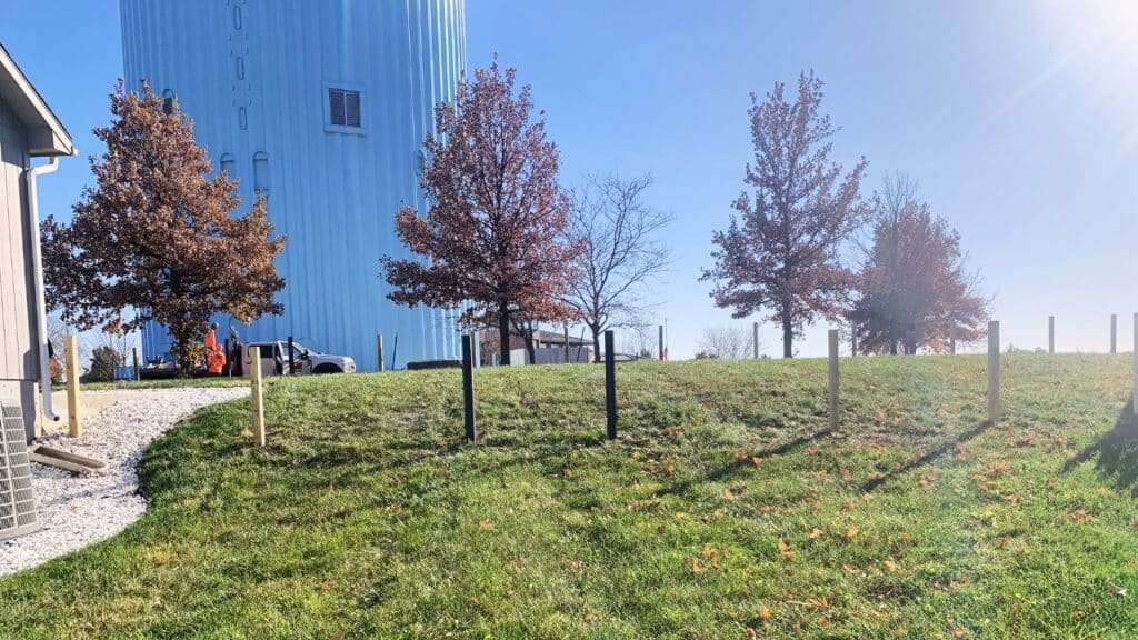 Row of newly set fence posts on a grassy hill, demonstrating proper post spacing for a residential fencing installation project.