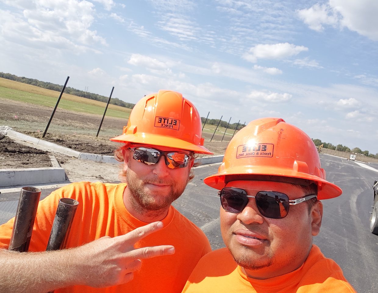 Two Elite Fence crew members in orange Elite hard hats at a job site