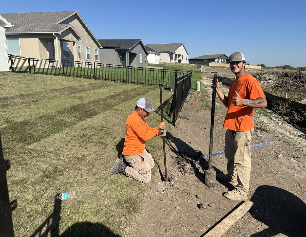 Two Elite Fence crew members smiling while setting a black ornamental fence post