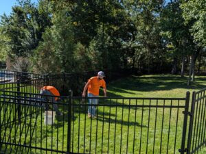 Elite Fence crew installing a black ornamental steel fence in a tree-lined backyard.