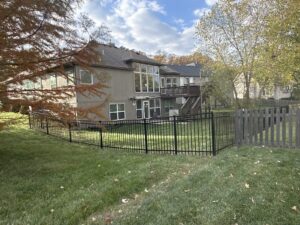 Black ornamental steel fence around a backyard below a two-story home in fall.