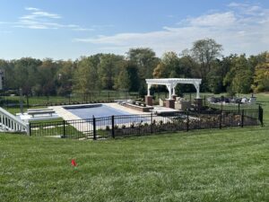 Black ornamental steel fence enclosing a backyard pool, patio and white pergola.
